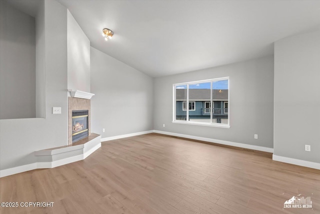 unfurnished living room with visible vents, a fireplace, vaulted ceiling, wood finished floors, and baseboards
