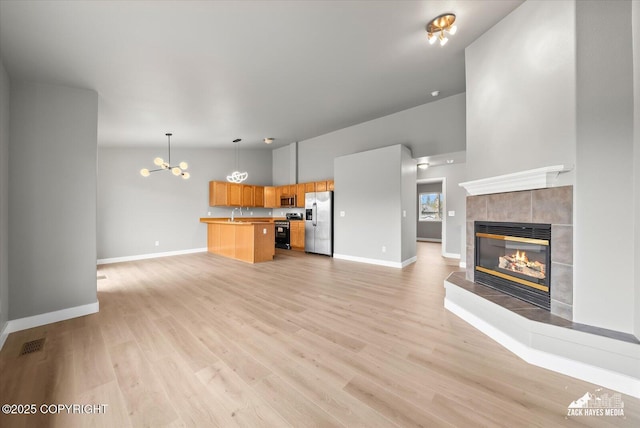 unfurnished living room featuring baseboards, an inviting chandelier, light wood-type flooring, and a tile fireplace