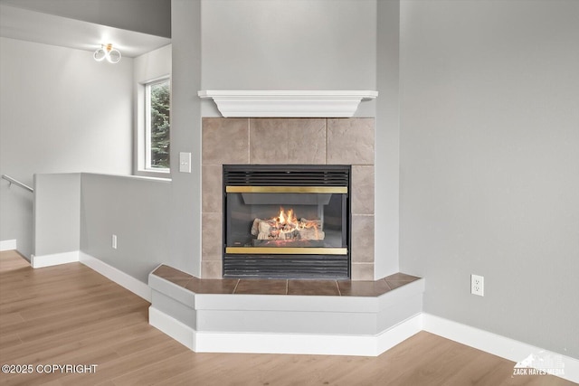 room details featuring baseboards, a tile fireplace, and wood finished floors