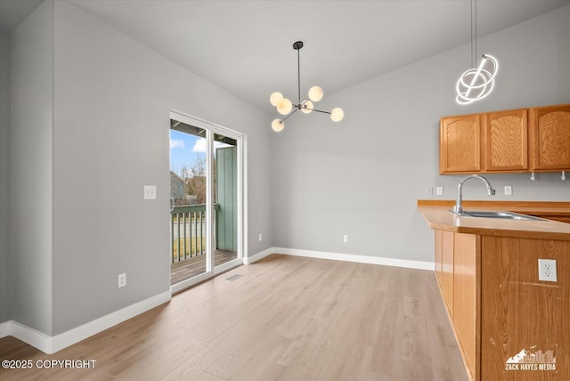 kitchen with vaulted ceiling, a sink, baseboards, light wood finished floors, and a notable chandelier