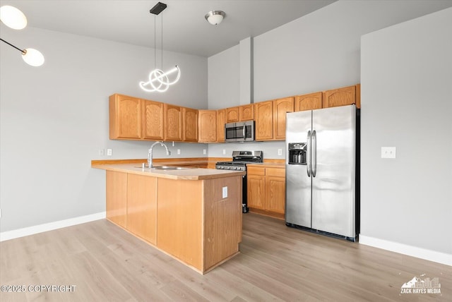 kitchen featuring a towering ceiling, appliances with stainless steel finishes, a sink, a peninsula, and light wood-style flooring