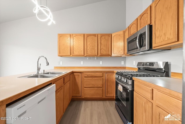 kitchen featuring a peninsula, light countertops, a sink, light wood finished floors, and appliances with stainless steel finishes