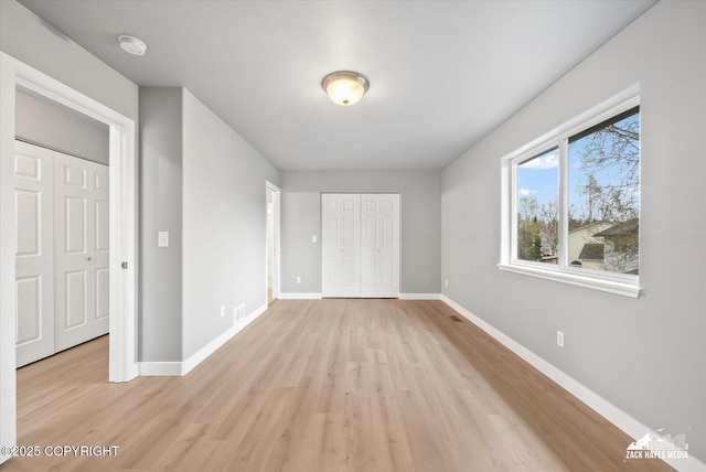 unfurnished bedroom with light wood-style floors, baseboards, visible vents, and a closet