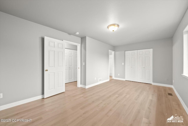 unfurnished bedroom with baseboards, a closet, light wood finished floors, and visible vents
