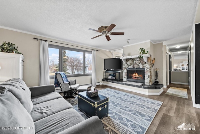 living area with ceiling fan, a textured ceiling, a stone fireplace, wood finished floors, and ornamental molding