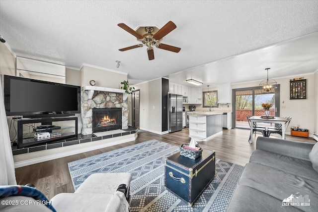 living area with a textured ceiling, a stone fireplace, ceiling fan with notable chandelier, and wood finished floors