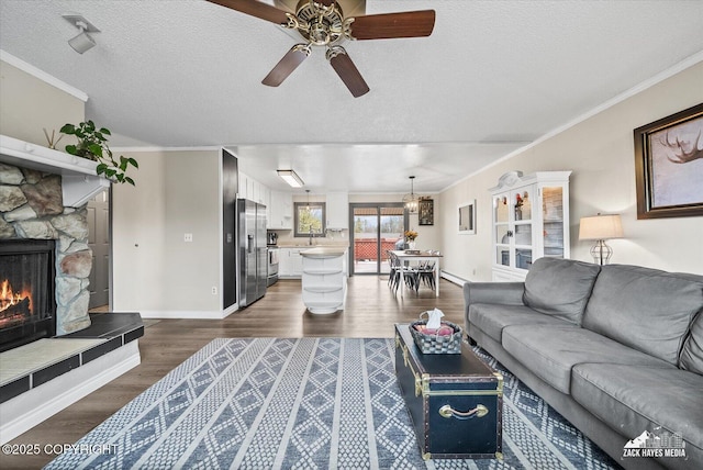 living room with ceiling fan, a stone fireplace, a textured ceiling, baseboards, and dark wood-style floors