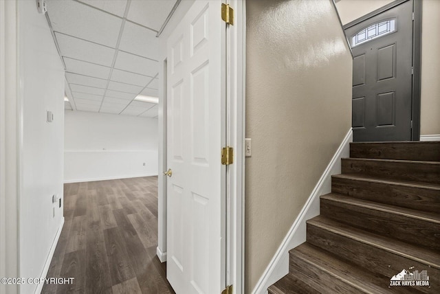 staircase featuring baseboards, a drop ceiling, and wood finished floors