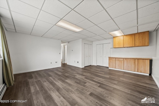 unfurnished living room with dark wood-style flooring, baseboards, and a drop ceiling