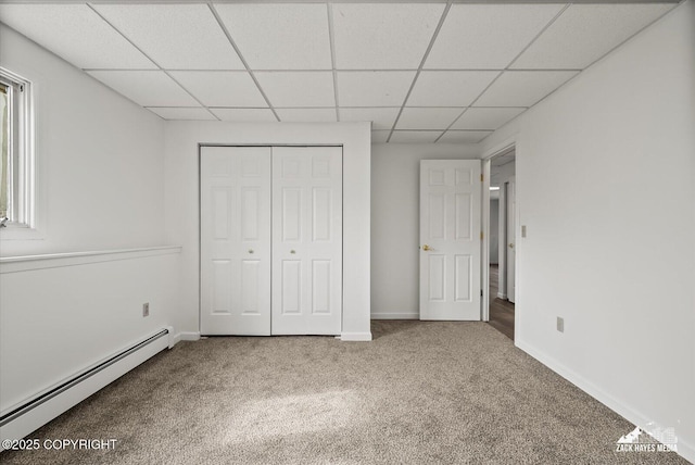 unfurnished bedroom featuring carpet floors, a paneled ceiling, baseboards, a baseboard radiator, and a closet