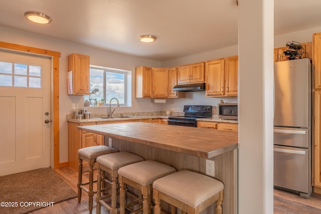 kitchen with stainless steel appliances, under cabinet range hood, a sink, wooden counters, and light wood-type flooring