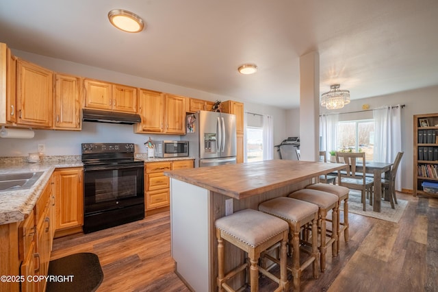 kitchen featuring appliances with stainless steel finishes, under cabinet range hood, dark wood-style flooring, and a kitchen breakfast bar