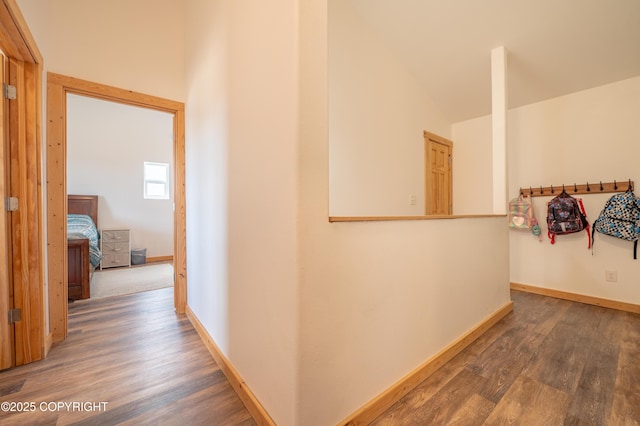 hallway featuring wood finished floors, vaulted ceiling, and baseboards