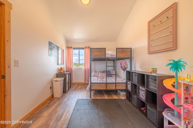 bedroom with vaulted ceiling, wood finished floors, and baseboards