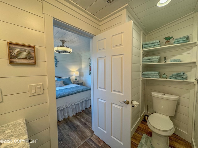 bathroom featuring wooden walls, toilet, and wood finished floors