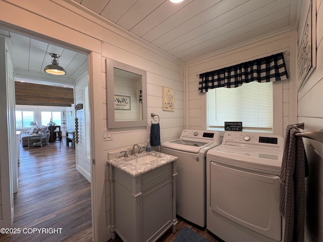 clothes washing area featuring laundry area, dark wood-style flooring, wood walls, a sink, and separate washer and dryer