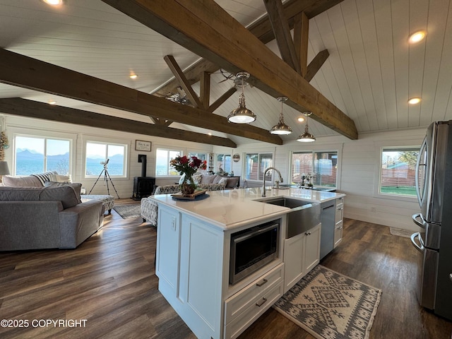 kitchen with a wood stove, open floor plan, white cabinets, a sink, and appliances with stainless steel finishes