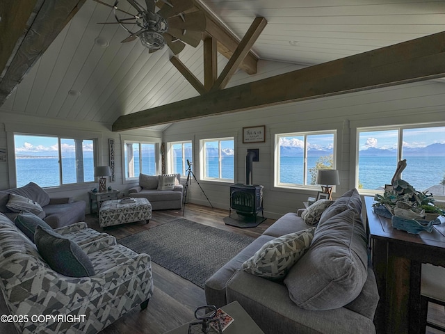 living area with ceiling fan, a wood stove, wood finished floors, beamed ceiling, and a water view
