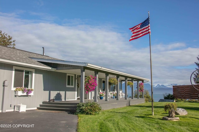 exterior space with covered porch, a lawn, a shingled roof, and a mountain view