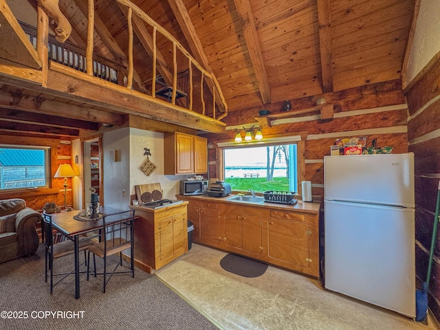 kitchen featuring brown cabinetry, freestanding refrigerator, stainless steel microwave, wooden ceiling, and a sink