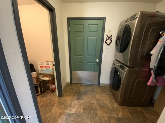 laundry room with baseboards, laundry area, stacked washer / drying machine, and stone finish floor