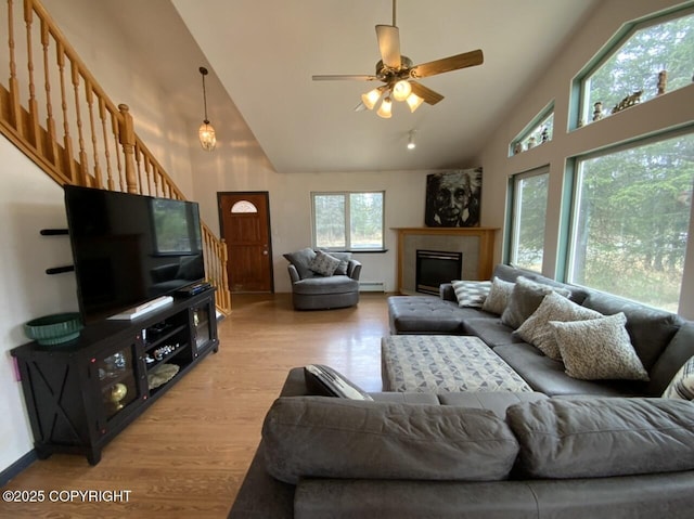 living room featuring a ceiling fan, high vaulted ceiling, a baseboard radiator, light wood finished floors, and stairs