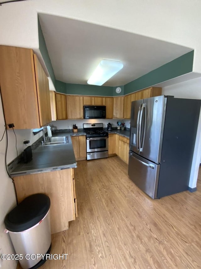 kitchen featuring dark countertops, a sink, light wood finished floors, brown cabinetry, and stainless steel appliances