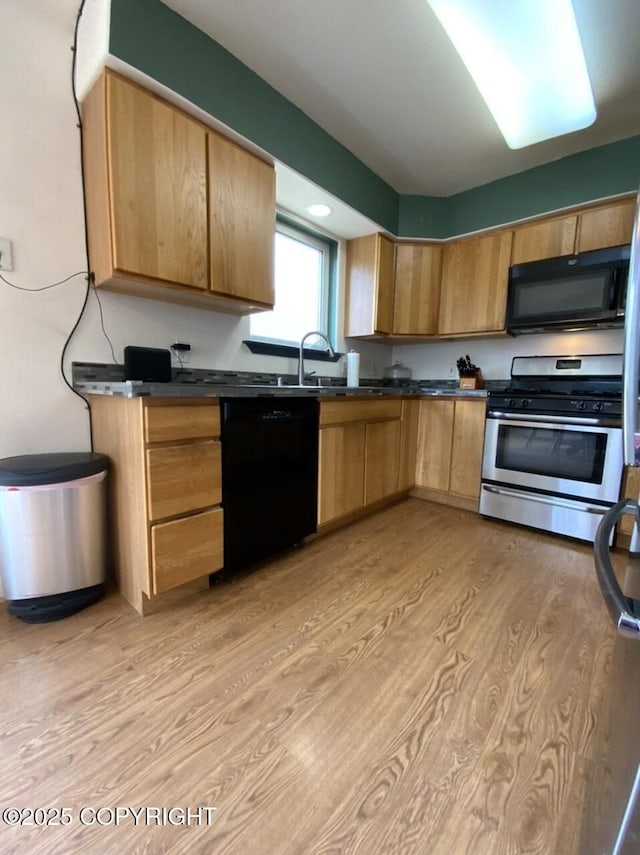 kitchen with a sink, dark countertops, black appliances, and light wood-type flooring