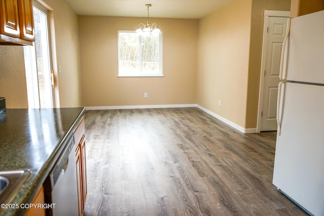 unfurnished dining area with a sink, an inviting chandelier, baseboards, and dark wood finished floors