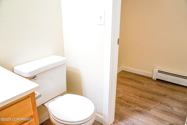 bathroom featuring baseboard heating, toilet, baseboards, vanity, and wood finished floors