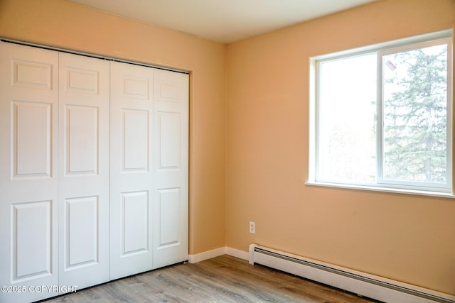 unfurnished bedroom featuring wood finished floors, a closet, baseboards, and a baseboard heating unit