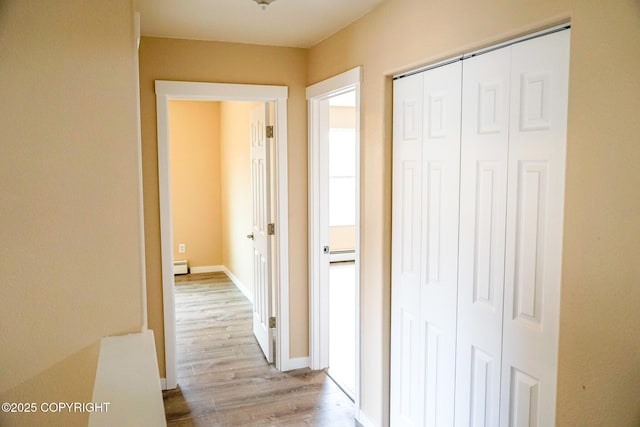 hall featuring baseboards, baseboard heating, and light wood-style floors