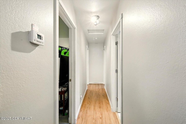 hall with a textured wall, baseboards, and light wood-style floors