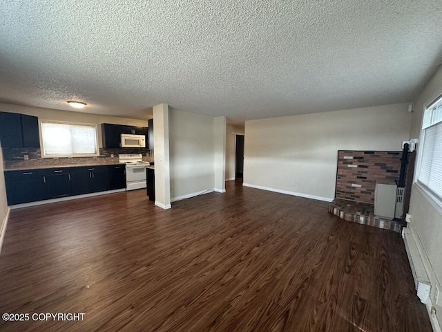unfurnished living room featuring baseboards, a wood stove, a textured ceiling, and dark wood-type flooring