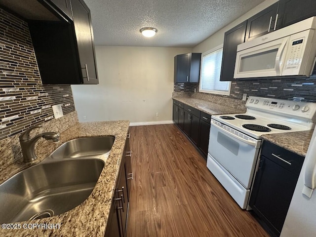 kitchen featuring a sink, white appliances, dark cabinetry, baseboards, and tasteful backsplash