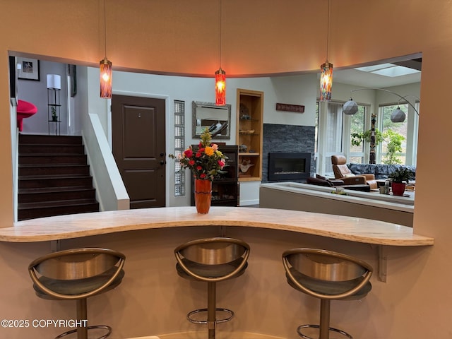 kitchen with a stone fireplace, pendant lighting, wood counters, and a kitchen breakfast bar