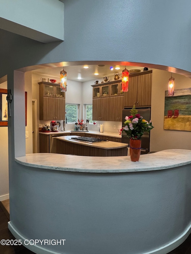 kitchen featuring light stone countertops, appliances with stainless steel finishes, brown cabinetry, and glass insert cabinets