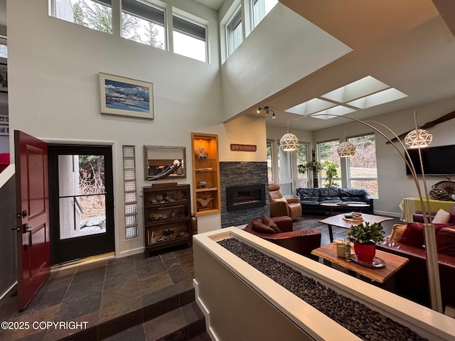 living room with a fireplace, a high ceiling, a healthy amount of sunlight, and a skylight