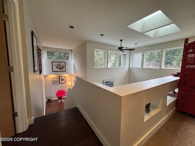 hall featuring baseboards, an upstairs landing, a healthy amount of sunlight, and a skylight