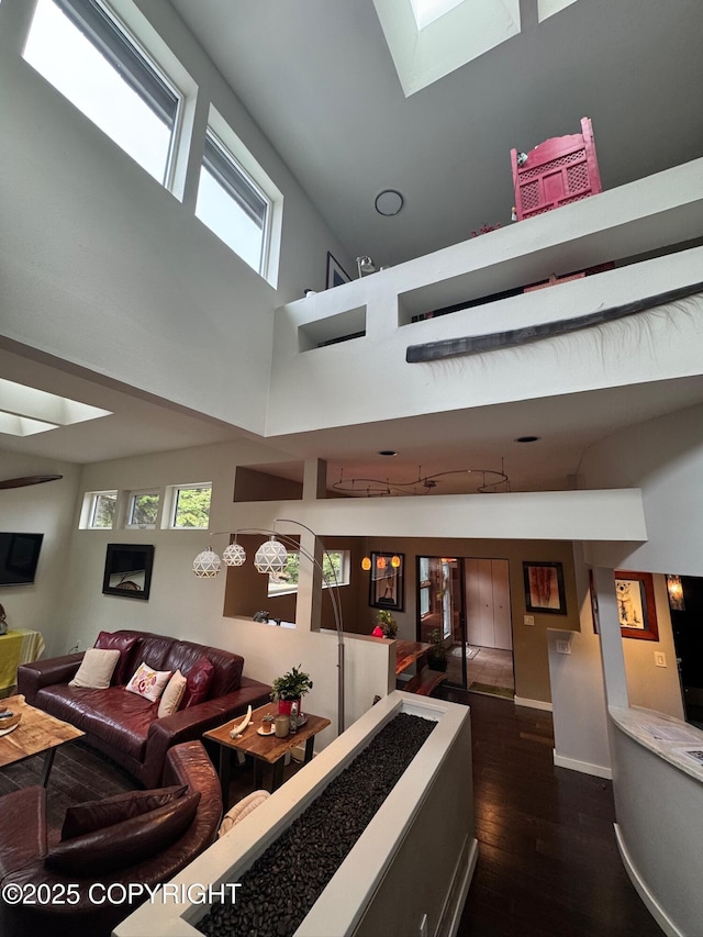 living area with a wealth of natural light, a high ceiling, dark wood-style floors, and a skylight