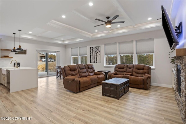living area with a stone fireplace, coffered ceiling, ceiling fan, and light wood finished floors