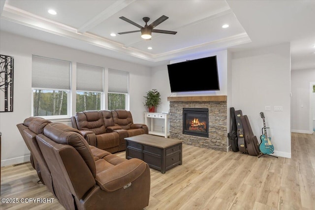 living area with a stone fireplace, a ceiling fan, light wood-style floors, and baseboards