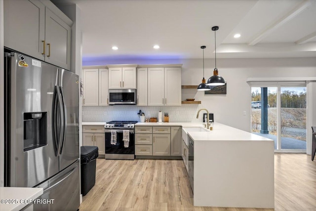 kitchen featuring a sink, light wood-style floors, stainless steel appliances, a peninsula, and tasteful backsplash
