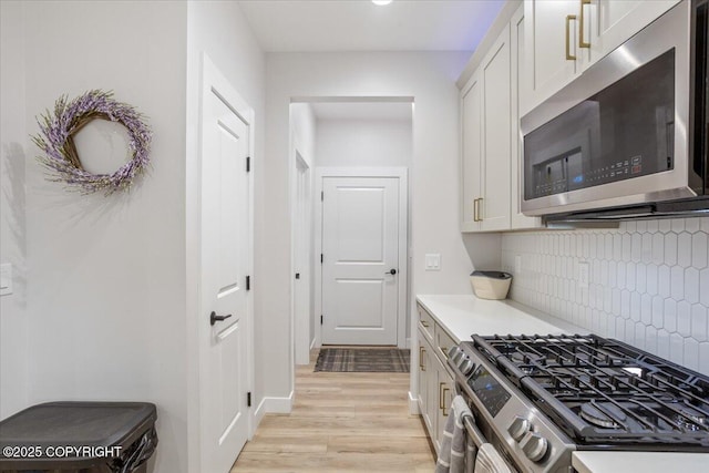 kitchen with decorative backsplash, appliances with stainless steel finishes, light countertops, light wood-style floors, and white cabinetry
