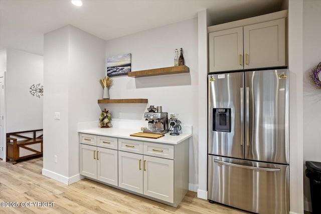 kitchen with open shelves, stainless steel fridge, light countertops, light wood-style flooring, and baseboards