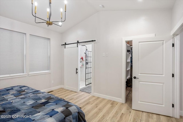 bedroom with a walk in closet, a barn door, wood finished floors, a chandelier, and lofted ceiling