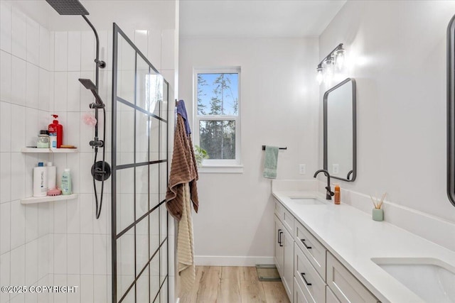 bathroom featuring double vanity, wood finished floors, a sink, baseboards, and tiled shower