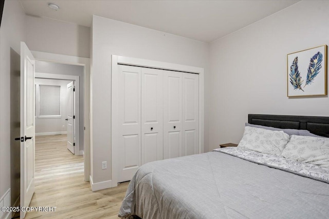 bedroom with light wood-style floors, baseboards, and a closet