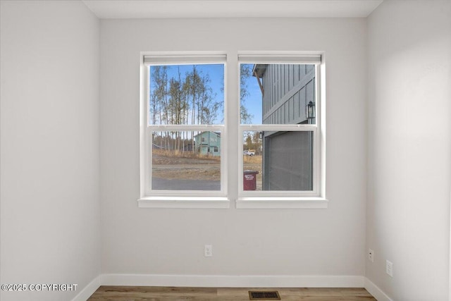 empty room featuring baseboards, wood finished floors, and visible vents