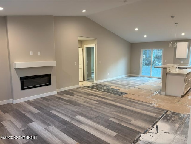unfurnished living room with a glass covered fireplace, recessed lighting, baseboards, vaulted ceiling, and light wood-type flooring
